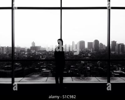 Silhouette di uomo che guarda fuori dalla finestra per vedere il paesaggio paesaggio - In bianco e nero Foto Stock