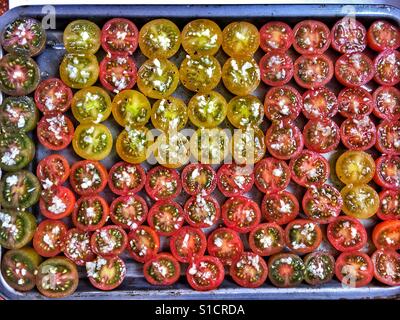 Varietà di pomodorini tagliati a metà e conditi con aglio, pronti per essere arrostiti. Foto Stock