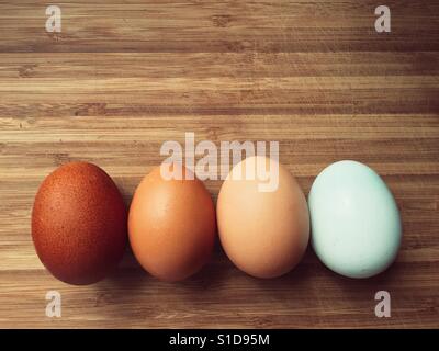 Quattro uova in diverse tonalità di colore su una superficie in legno Foto Stock