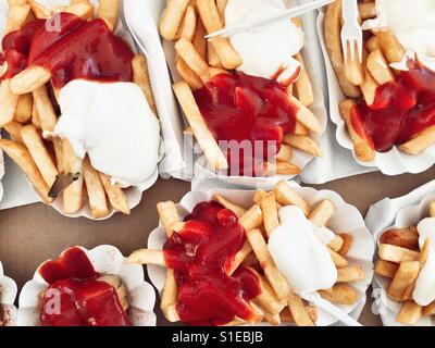 Piastre di carta di patate fritte con ketchup e maionese e salsiccia al curry Foto Stock