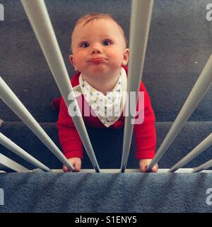 Otto mesi baby boy dietro una scala porta di sicurezza. Foto Stock
