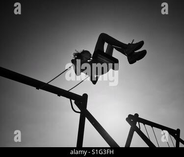 Giovane ragazza alta oscillante sul parco giochi altalena in silhouette contro il sole Foto Stock