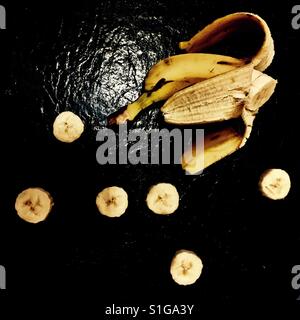 Mezza banana e fette di banana su sfondo nero Foto Stock