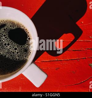 Un overhead di close-up shot di una nuova tazza di caffè nero su rosso di un tavolo di legno. Una composizione semplice con un ombra scura Foto Stock