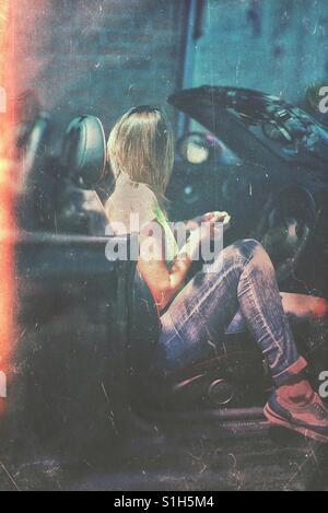 Giovane donna seduta in una vettura convertibile Foto Stock