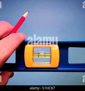 Un'immagine ravvicinata di un uomo con il livello di un falegname e una matita rossa contro uno sfondo blu Foto Stock