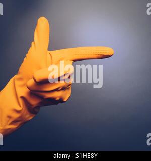 Una mano d'uomo in giallo di un guanto di gomma facendo una mano di puntamento gesto contro uno sfondo blu Foto Stock