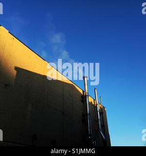 Bianco di sbuffi di fumo tubi di utilità al di fuori del palazzo giallo Foto Stock