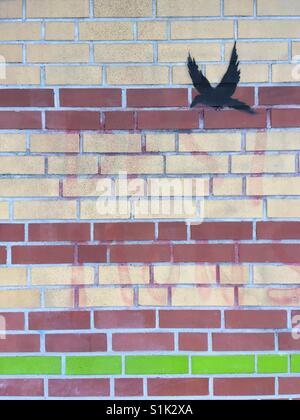 Stencil nero graffiti di un uccello in volo su un muro di mattoni a Bremen, Germania Foto Stock