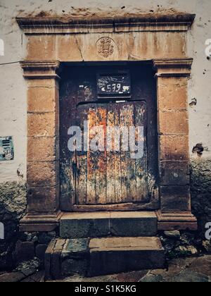 Un vecchio weathered pesante porta di legno con la pietra di involucro e fregio e cornicione e grandi passi in Cusco, Perù Foto Stock