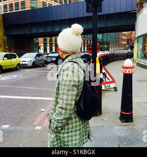 Donna pedonale in attesa di cross Street a Londra indossando Cappello invernale Foto Stock