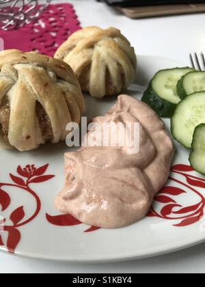 Tritata cotta al forno polpettine di carne avvolti in strisce di pasta sfoglia. Cluster di carni macinate e di pasta. Esse giacciono su una piastra. Successivamente, ​​cucumbers affettato e salsa. Foto Stock