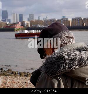 Senior uomo con tappo piatto testa piegata a piedi lungo il fiume Tamigi foreshore Londra Foto Stock