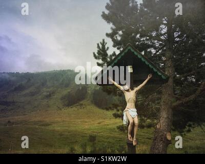 Una rappresentazione di Gesù Cristo sulla croce con una montagna e nuvole in background Foto Stock