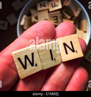 Un'immagine ravvicinata di una mano di un uomo azienda lettere in legno ortografia vincere con altre lettere in legno in background Foto Stock