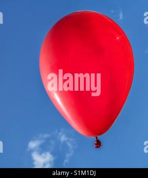 Foto verticale di un colore rosso brillante balloon floating contro un cielo blu con piccole nuvole bianche Foto Stock