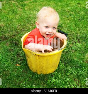 Undici mesi di età bambino seduto in un secchio di acqua sporca Foto Stock