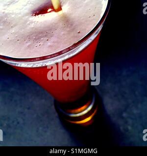 Close up di birra che viene versata in un bicchiere pieno su una superficie di cemento Foto Stock