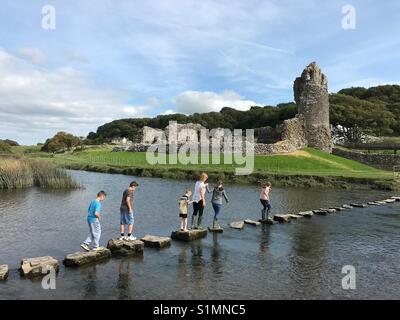 Il XII secolo il castello di Ogmore Galles del Sud, con la gente che camminava sulle pietre miliari attraverso il fiume Ogmore Foto Stock