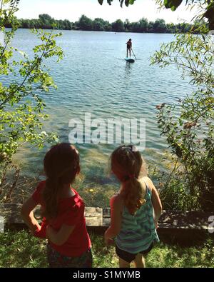 Little girls watching paddle boarder sul lago Foto Stock