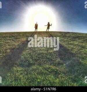 I due ragazzi in piedi sulla cima di una collina di grandi dimensioni con sfolgorante sole dietro di loro. Foto Stock