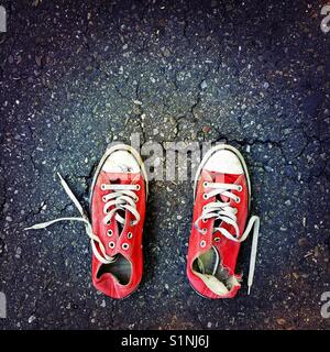 Un vecchio usurato coppia di red Converse sneakers su un manto di asfalto Foto Stock