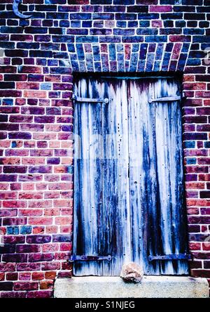 Persiane di legno nel vecchio edificio di mattoni con letti in ferro battuto con cerniere Foto Stock