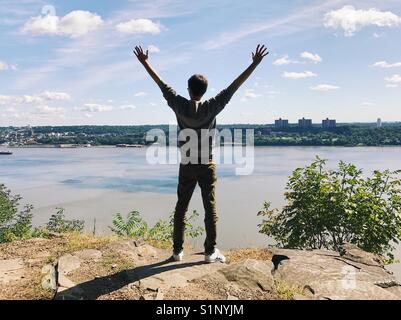 Un uomo con le braccia aperte, in piedi sul new jersey palisades affacciato sul fiume Hudson e New York. Foto Stock