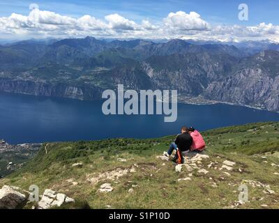Due persone sedersi sul Monte Baldo, Italia guardando in giù sul Lago di Garda, con la città di Limone in background Foto Stock