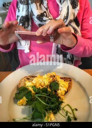 Donna prendendo una foto dello smartphone della sua prima colazione, uova strapazzate su pane tostato Foto Stock