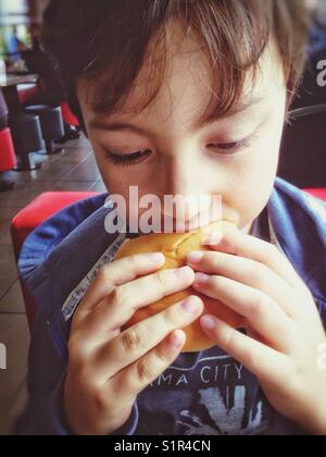 Un ragazzo di prendere un boccone fuori di un hamburger. Foto Stock