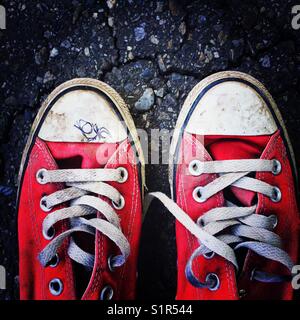 Close up dettaglio di una vecchia coppia di tela rossa sneakers su un manto di asfalto Foto Stock