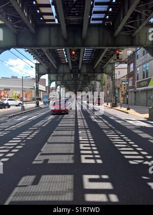 Vetture passando sotto la metropolitana sopraelevata linea su Broadway Ave a Brooklyn, New York Foto Stock