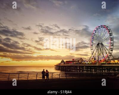 Due persone a guardare il tramonto dal accanto alla centrale illuminata Pier di Blackpool Foto Stock