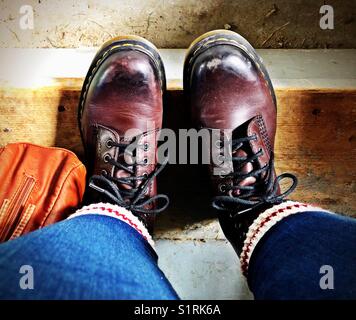 Vista Selfie di seduta su una schifezza passo in legno marrone da indossare stivali in pelle, Calzini termici e blue jeans skinny Foto Stock