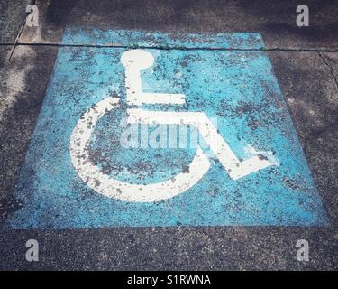 Disabilitare il simbolo della carrozzella stencil in bianco sul quadrato blu nel parcheggio. closeup segno di comunicazione sulla disabilità parcheggio auto. Foto Stock