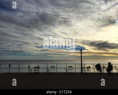 Le persone siedono lungo la Promenade a Seaton beach nel Devon, in Inghilterra il 13 novembre 2017 Foto Stock