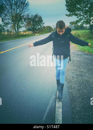 Ragazza che cammina sulla linea dipinta lungo il lato della strada nel sud dell'Ontario, Canada Foto Stock