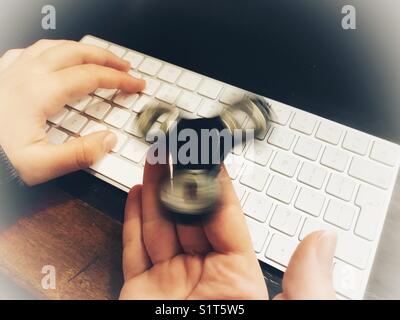 Agitano: spinner, filatura su un milennial la mano, mentre seduti ad un cuoio sormontato scrivania con una mano su un computer wireless tastiera. Foto Stock