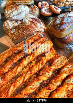 Formaggi, cannucce e diversi tipi di pane e pasticcini in mostra in una vetrina di un negozio di panetteria Foto Stock