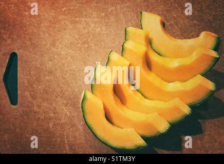 Fette di melone cantaloupe ben disposte su un tagliere marrone Foto Stock