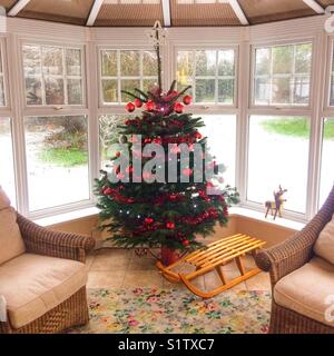 Albero di Natale vero in una veranda decorata con red baubles, con neve sul terreno al di fuori. Hampshire, Inghilterra, Regno Unito. Foto Stock