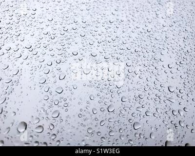 Gocce di pioggia su una finestra contro un cielo grigio Foto Stock