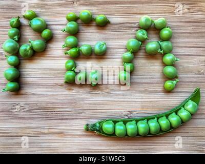 Fresco verde piselli in un pod e piselli l'ortografia della parola pisello, su una scheda di bambù con spazio di copia Foto Stock