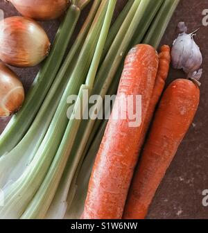 Ortaggi freschi consistente di cipolle, sedano, carote e aglio su un marrone tagliere Foto Stock