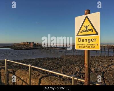 Un segno di avvertimento di forti correnti con Birnbeck Pier, Weston-super-Mare, Regno Unito in background. Foto Stock