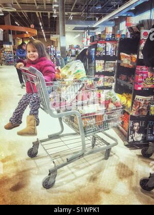 Bambina di equitazione in pieno carrello di generi alimentari nel supermercato Foto Stock