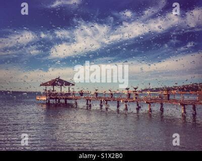 Guardando attraverso una finestra con le gocce di pioggia, il beach bar sul pontile in background Foto Stock