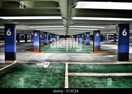 L'interno di livello 6 di un deserto multi storia parco auto con aspre luci colorate di illuminazione degli spazi di parcheggio e colonne Foto Stock