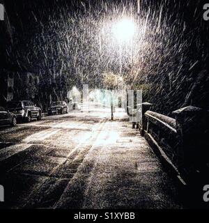 La neve cade passato un lampione di notte su una strada tranquilla Foto Stock
